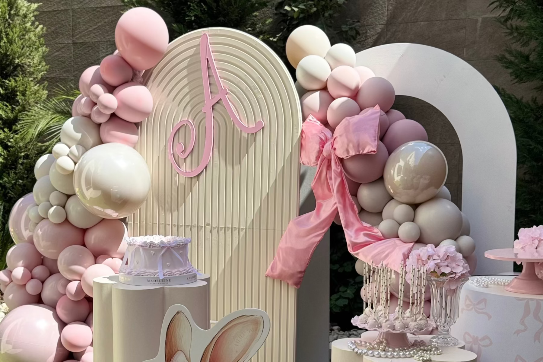 Decorative arch with pink and white balloons and a letter 'A' at a party.