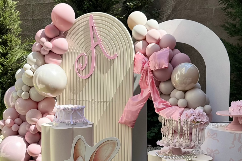 Decorative arch with pink and white balloons and a letter 'A' at a party.